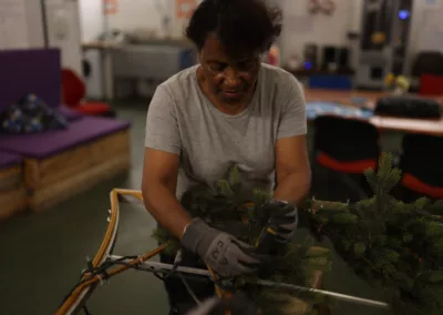 Blachère et Zou Vaï - Une femme portant des gants de travail assemble des branches d’un décor lumineux.