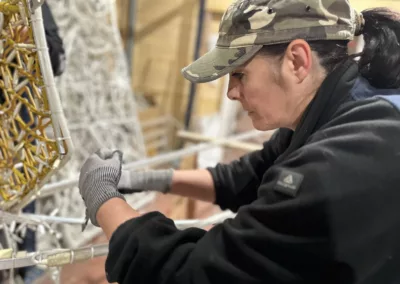 Une femme portant une casquette camouflée travaillant sur une structure décorative en métal.