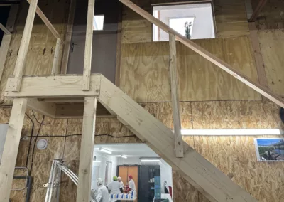 escalier en bois avec rampe menant a un bureau sur mezzanine avec des ouvriers en arriere plan travaillant dans un atelier