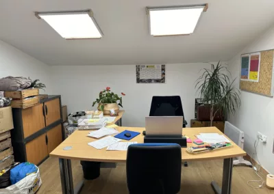 Nouveaux bureaux opérationnels - espace de travail sous une mezzanine avec un grand bureau une plante verte des etageres de rangement et une decoration murale