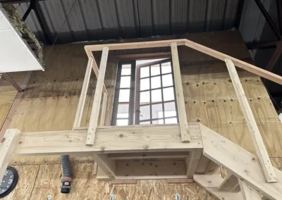 vue dun escalier en bois menant a une mezzanine avec une fenetre vitree dans un espace industriel en construction